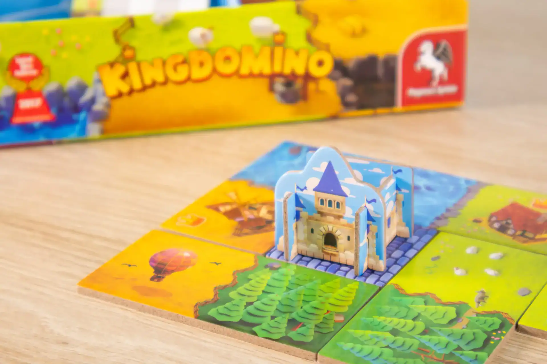 Kingdomino Spielset mit Burg, Spielplan und Landschaftsteilen, auf Holzoberfläche.